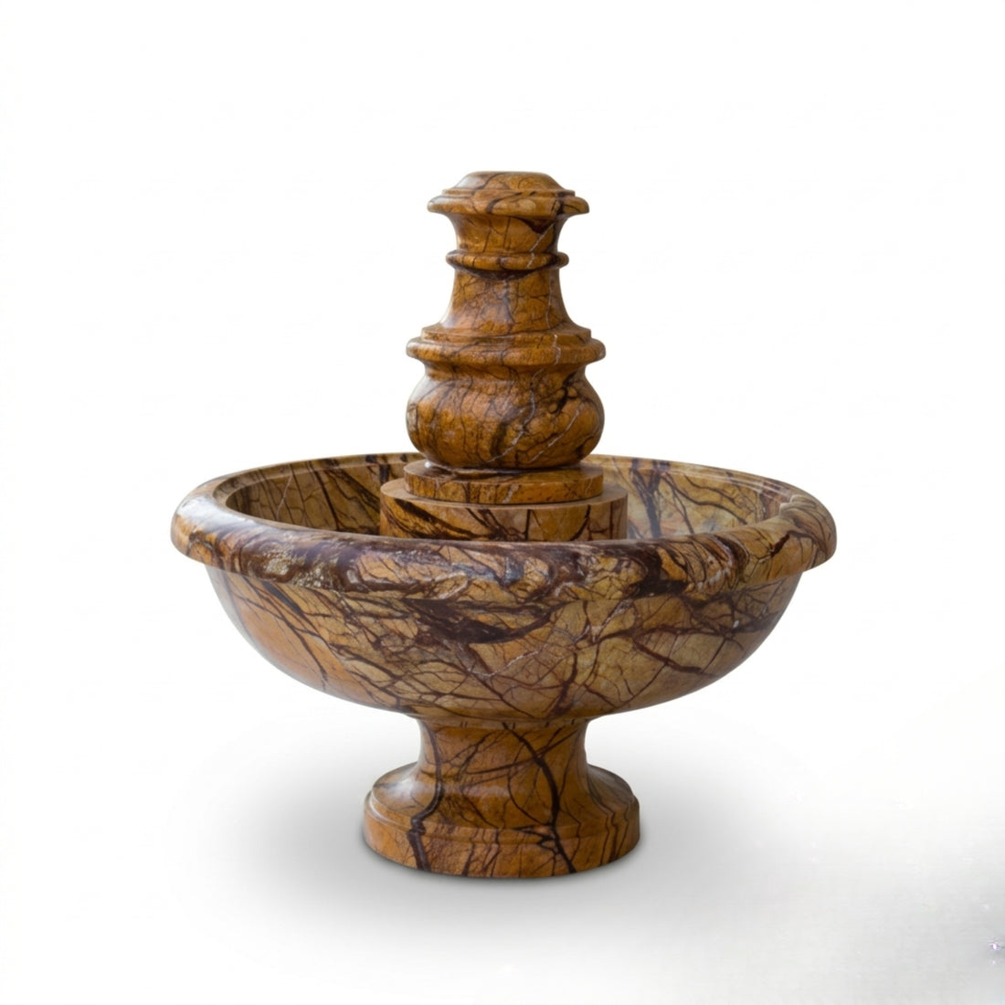 A tiered stone fountain with a warm golden-brown and dark brown marbled pattern, set in a modern outdoor courtyard with black river stones and manicured green shrubs.