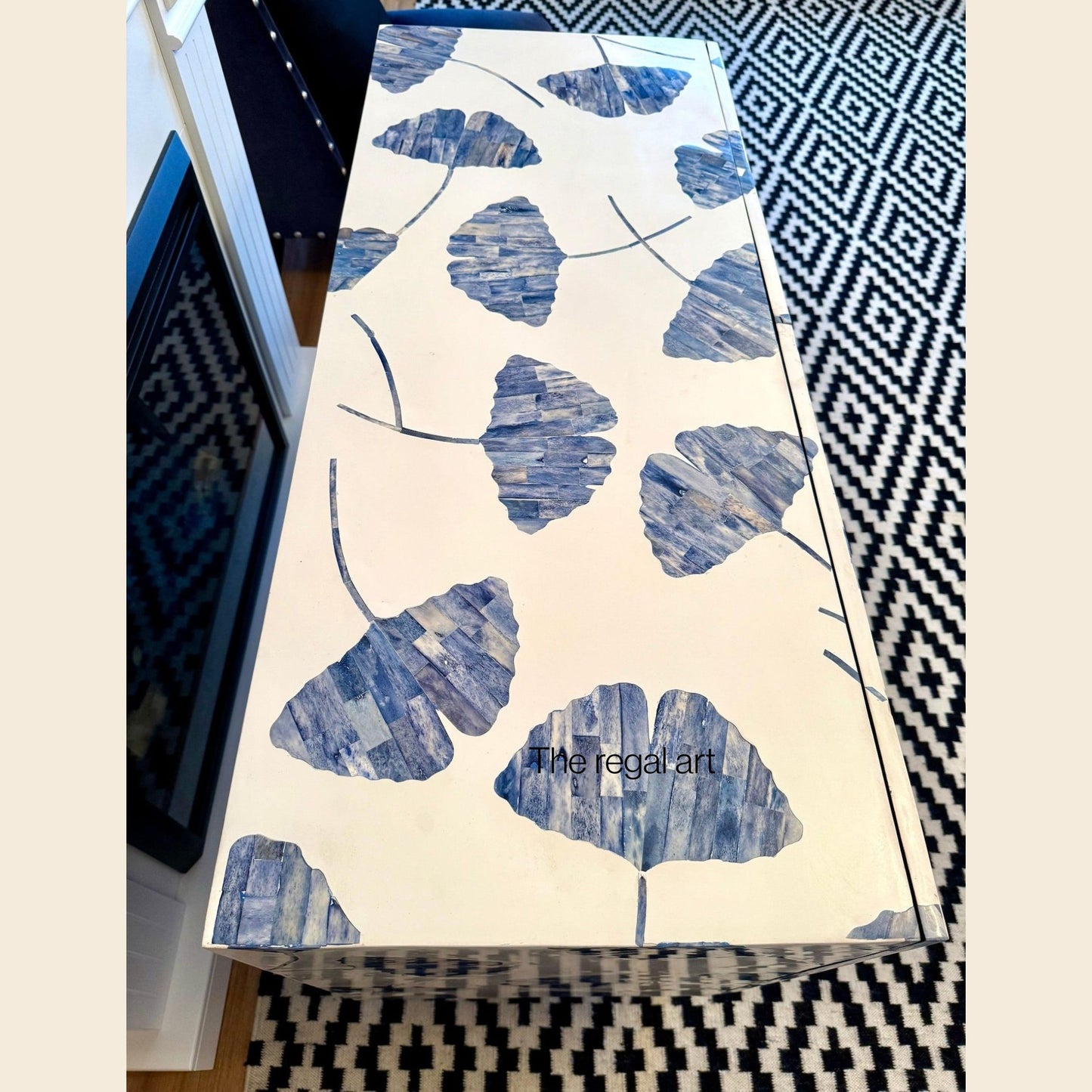 Table with blue leaf pattern and 'The Regal Art' branding on a geometric-patterned rug.