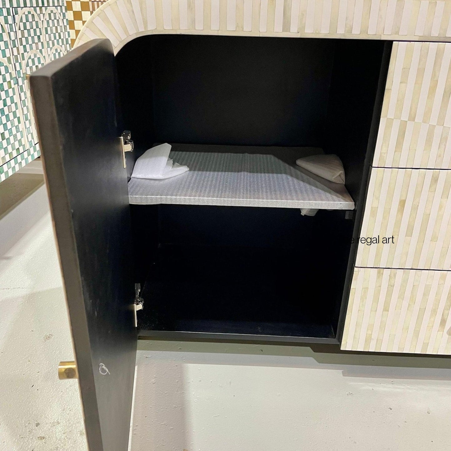 Cabinet with open door revealing a small bed inside, against a tiled wall.