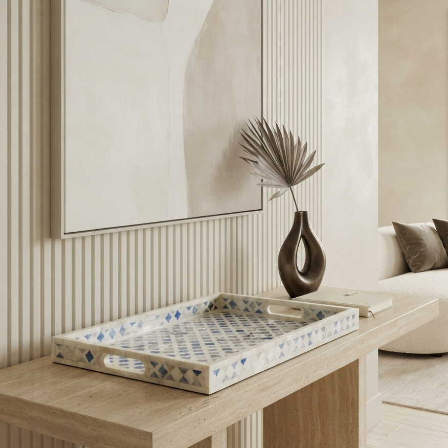 A rectangular decorative tray with blue geometric patterns on a cream base, styled on a light wood console table in a modern, neutral-toned living room.
